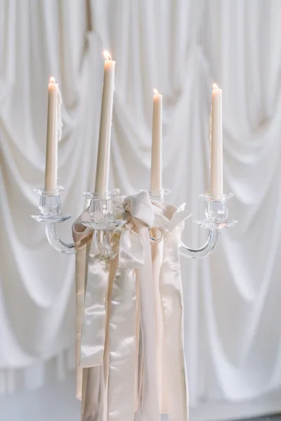 Wedding candelabra, a glass candelabra styled with ivory taper candles, stands before softly draped white curtains and fabric.