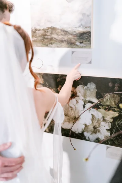 Couple portrait captures a candid couple moment, the groom holding the bride before a gallery wall, her soft tulle veil trailing behind.