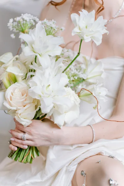 Bridal bouquet of all-white blooms, hand-tied with natural stems, held by a bride as her engagement ring catches the light.