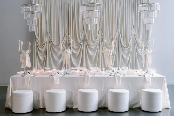 Reception tablescape as an all white reception table, featuring gleaming crystal glassware beneath softly draped curtains.