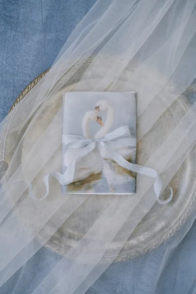 Wedding stationery with a swan motif invitation styled on a silver tray over blue fabric, showcasing hand-painted details.