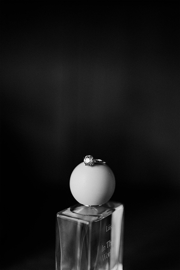 Engagement ring diamond solitaire ring resting on a perfume bottle, sparkling against a dark backdrop for a moody bridal detail flat lay