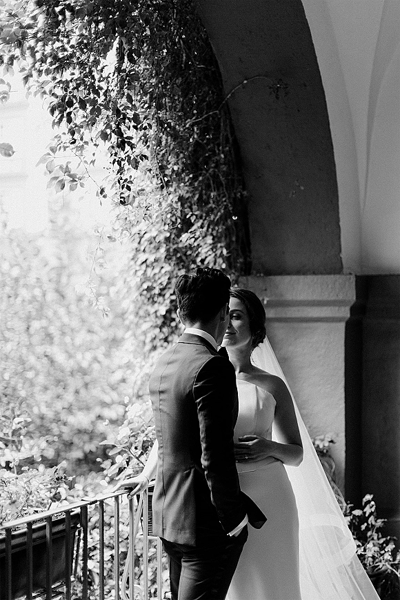 Wedding couple portrait in a black and white wedding portrait, bride and groom in close embrace under a stone ivy archway with veil drape