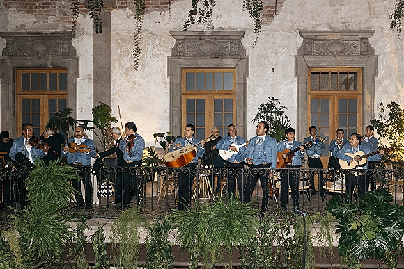 Wedding mariachi band performing on a balcony terrace, mariachi band wedding reception with violins, trumpets, and guitars by stucco walls