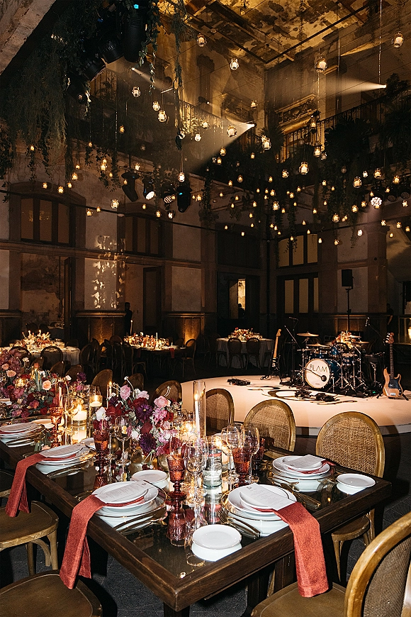 Reception tablescape with wedding head table decor, long floral centerpiece and taper candles on dark wood table in grand ballroom with stage lighting