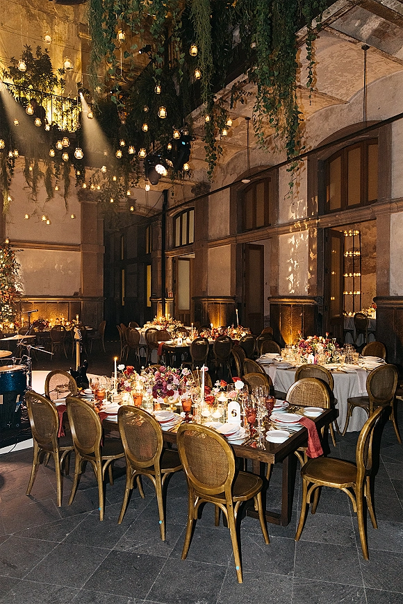 Reception tablescape with wedding reception table decor, taper candles and floral centerpieces under hanging jar lights in an industrial hall