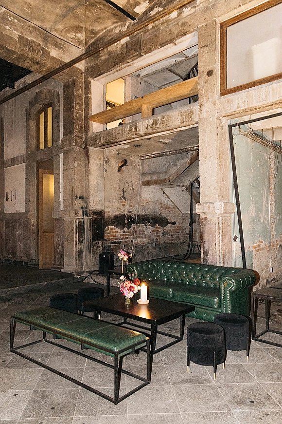 Wedding lounge area with green leather sofa, black coffee table, and pillar candle, set in an industrial loft with exposed brick and windows