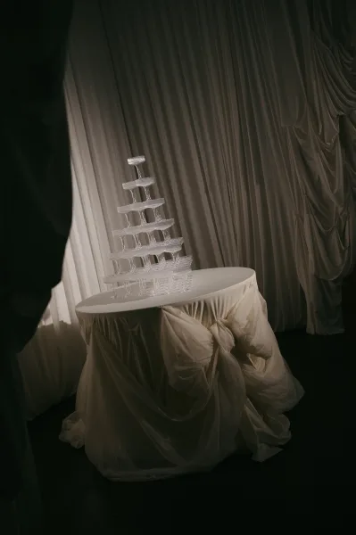 Champagne tower setup as a coupe glass pyramid with a draped tablecloth, set against a white drapery backdrop.