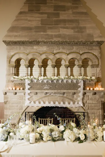 Fireplace wedding decor with reception mantel flowers, framed by an arched stone fireplace, glows with votive candles near a brick firebox.