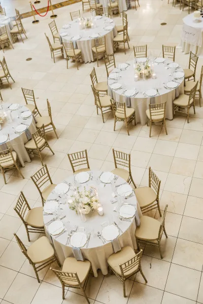 Reception tablescape for a round table reception with elegant gold chiavari chairs encircling neutrally styled tables in a cohesive layout