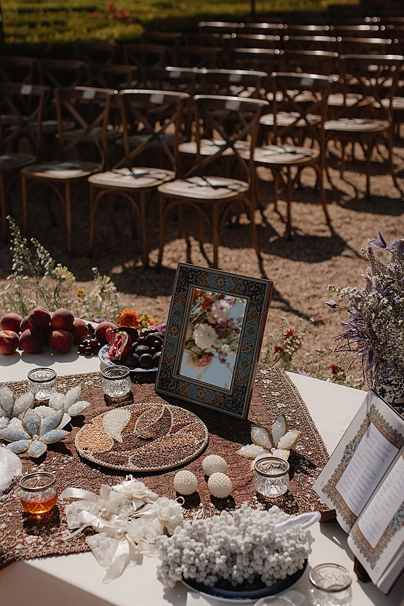 Ceremony welcome table with wedding welcome table decor, framed sign, votive candles, dried florals, and fruit platter in sunlight outdoors