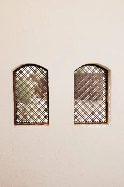 Venue architecture with arched window detail and lattice screens casting sunlit shadows on a white stucco wall with greenery nearby