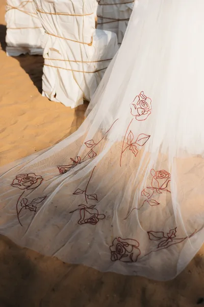 Wedding veil with embroidered wedding veil floral appliqué and red thread details draped over a chair on a sunlit stone floor