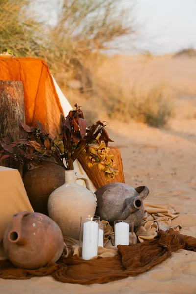 Wedding decor vignette with desert wedding decor in terracotta pots, ceramic jugs, orchids, dried foliage, and glass cylinder candles on sand