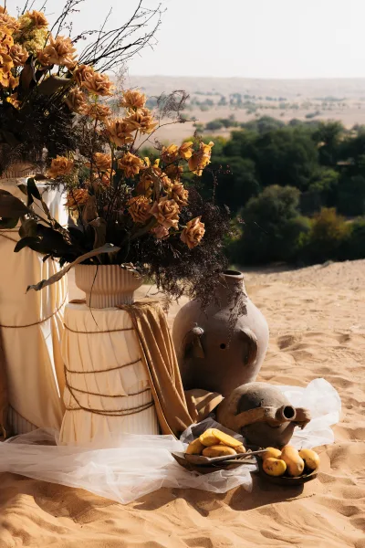 Ceremony decor with wedding ceremony floral arrangement of dried roses and branches in a ceramic vase on sand, with tulle drape and fruit accents