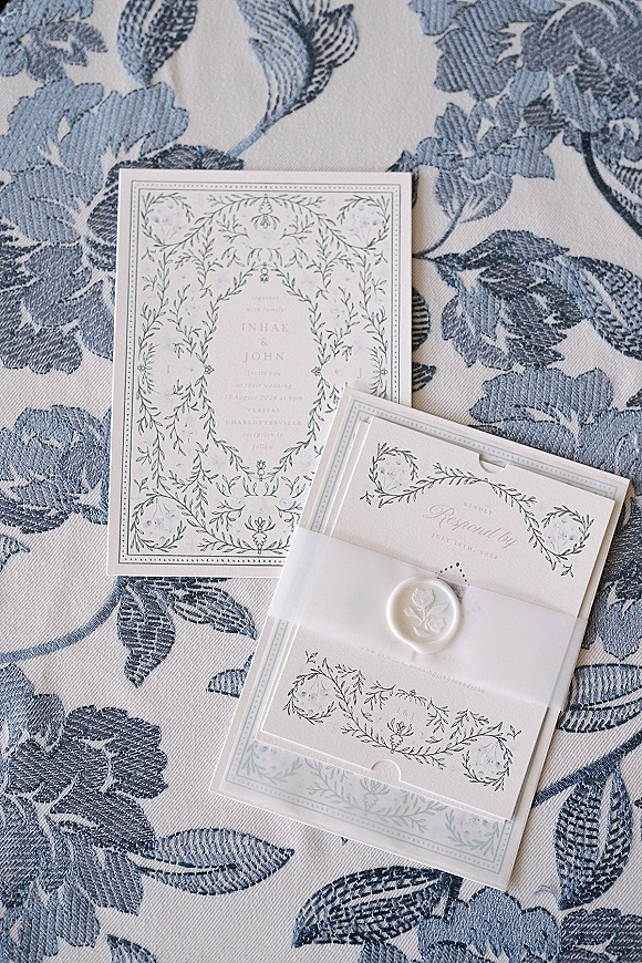 Wedding invitations arranged as a wedding invitation suite with RSVP card, vellum wrap, wax seal, and floral deckled paper on blue fabric