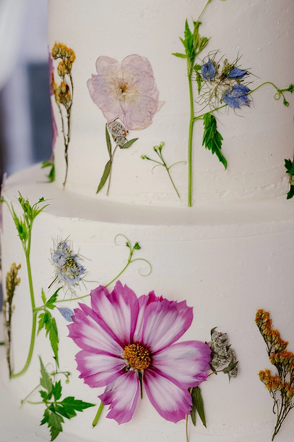 Wedding cake with pressed flower wedding cake accents, edible petals and green leaves on smooth white buttercream tiered design
