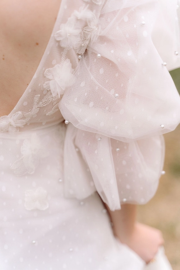 Wedding dress detail with pearl wedding dress beading on polka dot tulle and an oversized tulle bow, outdoor ground softly blurred behind