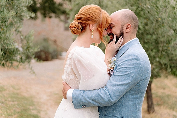 Wedding couple portrait of bride and groom embrace, forehead touching as she cups his face on a tree-lined path in soft light