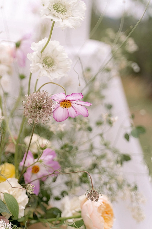 Wedding florals with wildflower wedding flowers, pink cosmos and blush rose accents nestled in greenery against a softly blurred garden backdrop