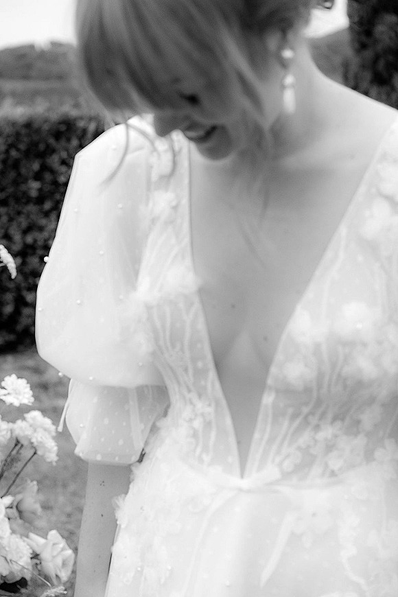 Wedding dress close-up showing lace wedding dress bodice with deep V neckline and sheer puff sleeves, beaded appliques, greenery behind