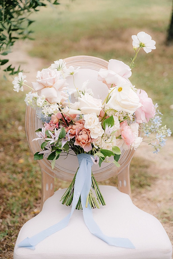 Wedding bouquet with pastel bridal bouquet blooms of roses, peonies and white cosmos, tied with a blue ribbon on a chair outdoors