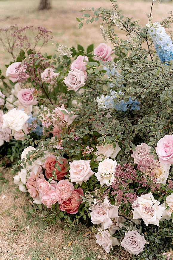 Wedding flowers in a ceremony floral arrangement on a grass lawn, with roses, hydrangea, and lush greenery in soft pastels