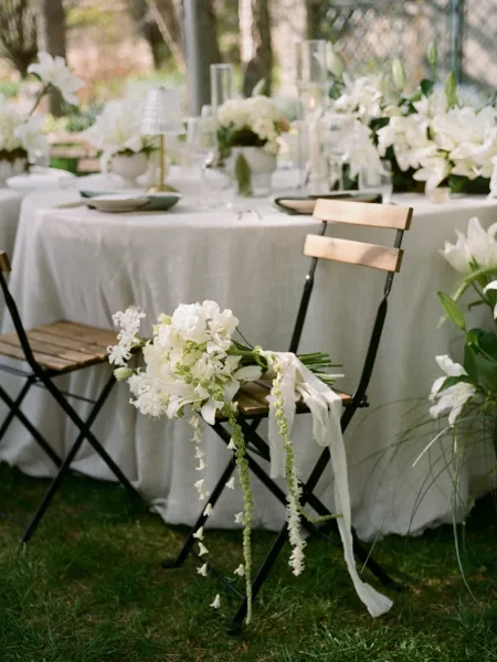 Reception tablescape, outdoor wedding tablescape with white floral centerpiece and taper candles on a white linen table on a garden lawn