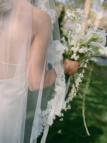 Bridal bouquet, white lily bouquet with trailing white lilies beside a lace wedding veil on green grass in soft outdoor light