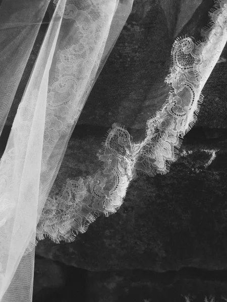 Lace wedding veil with cathedral lace veil scalloped trim and sheer tulle spread on a dark fabric surface, highlighting delicate embroidery detail