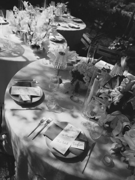Reception tablescape with a wedding place setting, menus and place cards, lilies, taper candles, and a small table lamp amid greenery