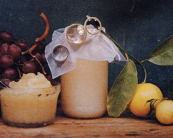 Wedding rings and engagement ring close up on a ring box with a diamond solitaire, grapes and leaves on a dark wood surface