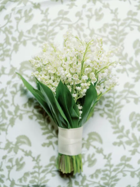 Bridal bouquet with lily of the valley flowers and green leaves, wrapped in white ribbon, arranged on patterned wallpaper background