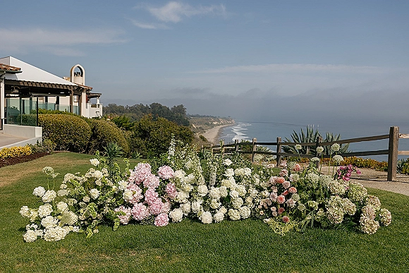Wedding ceremony florals and ceremony floral meadow of hydrangeas, roses, and greenery on a cliffside lawn overlooking the ocean coast