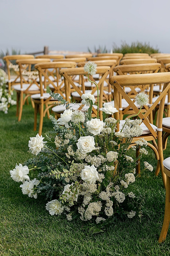 Ceremony aisle decor with outdoor ceremony chairs, white roses and ranunculus along a grass aisle overlooking the ocean view