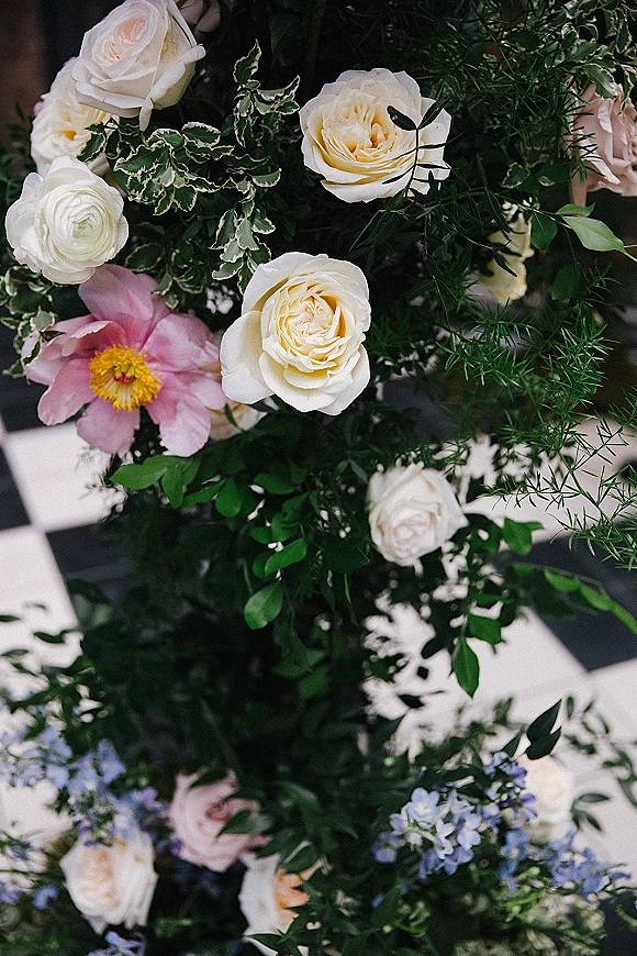 Wedding bouquet of white roses with a pink peony and blue flowers nestled in lush greenery, photographed close up against a soft blurred background