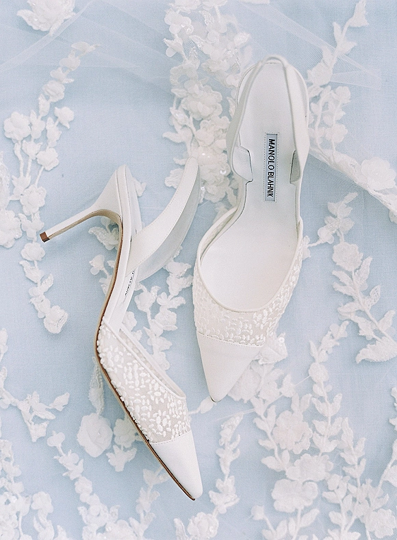 Bridal shoes, white slingback heels with lace appliqué and pointed toes, styled on lace wedding fabric with soft tulle overlay