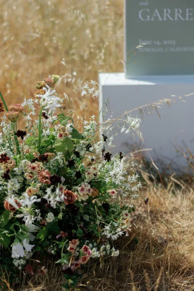 Wedding welcome sign on a white pedestal plinth with welcome sign with flowers, wildflower accent, set in a tall dry grass meadow