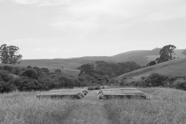 Ceremony seating with outdoor wedding ceremony seating on wood benches, an aisle lined with florals in a grassy field with rolling hills