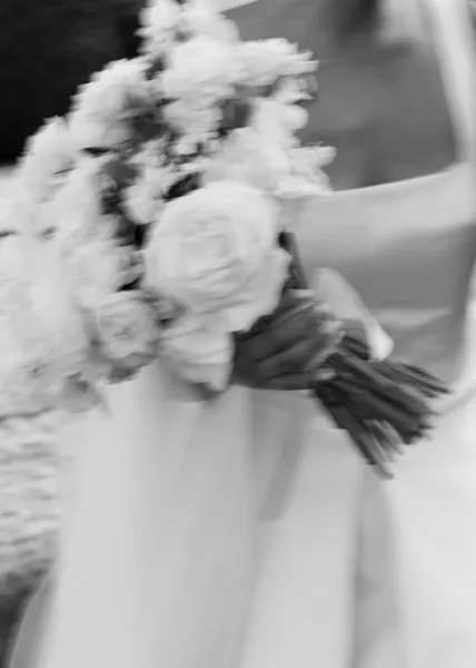 Bridal bouquet of white rose bouquet blooms wrapped with a ribbon, held against a bridal gown with a softly blurred interior background