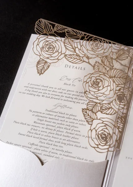 Wedding invitation suite with laser cut wedding invitation floral wrap, details card and envelope arranged on a black fabric backdrop