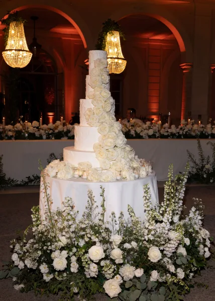 Wedding cake with a tall tiered wedding cake design, sugar rose cascade on a candlelit table beneath crystal chandeliers in an arched room