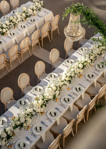 Reception tablescape long table wedding reception with white floral garland, greenery, taper candles, and crystal chandelier on an outdoor patio