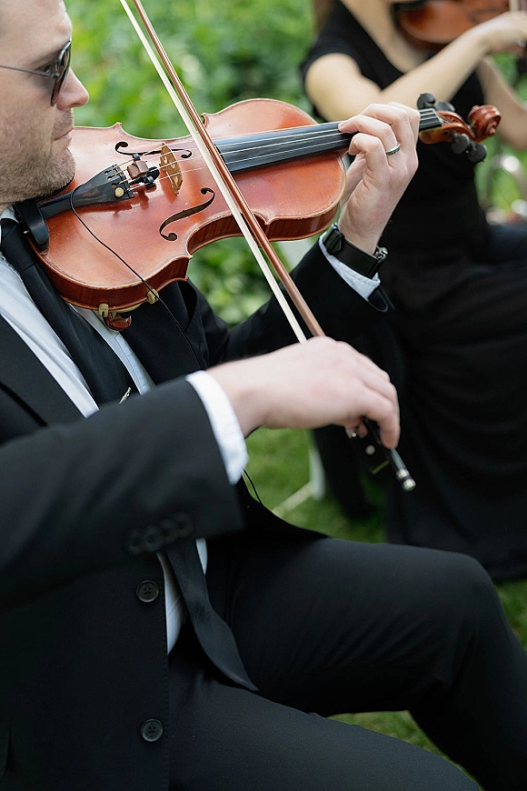 Wedding violinist playing live string quartet wedding music outdoors, in a black suit with sunglasses and wedding band on a green lawn