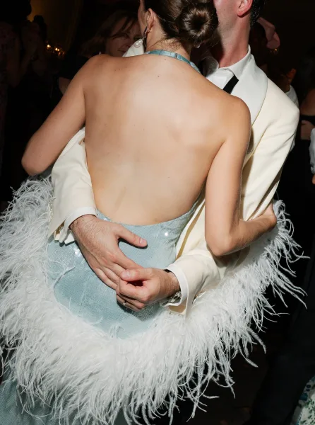 Couple dancing in a close embrace during a wedding reception dance, the bride’s pearl earrings catching ambient indoor lights as guests look on.