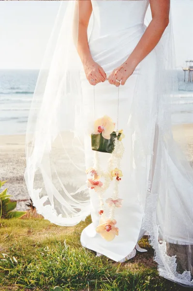 Bouquet alternative: a floral purse trimmed with orchids on a beach, with ocean waves and dune grass stretching behind.