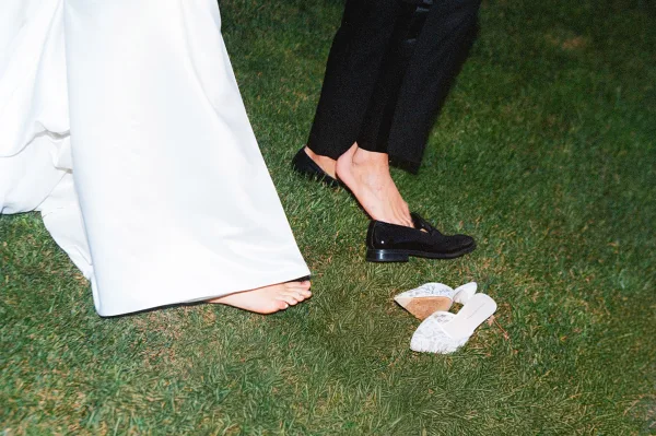 Reception moment with a bride barefoot on the grass lawn, her lace heels dropped nearby as she strolls, relaxed and playful.