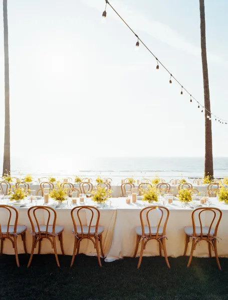 Reception tablescape showcasing outdoor wedding reception decor, anchored by string lights on a seaside lawn with ocean views and palm trees.