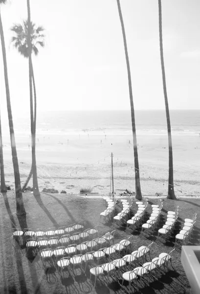 Beach ceremony setup with outdoor ceremony seating on a grass lawn, string lights overhead, palm trees framing the ocean horizon.