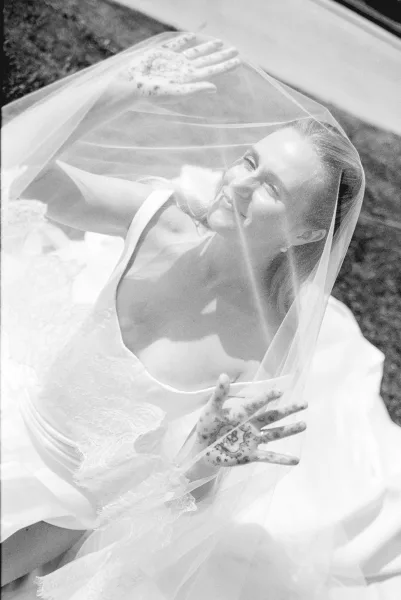 Bridal portrait of a bride under a veil, smiling softly as she frames her face with the veil, focus on serene expression.